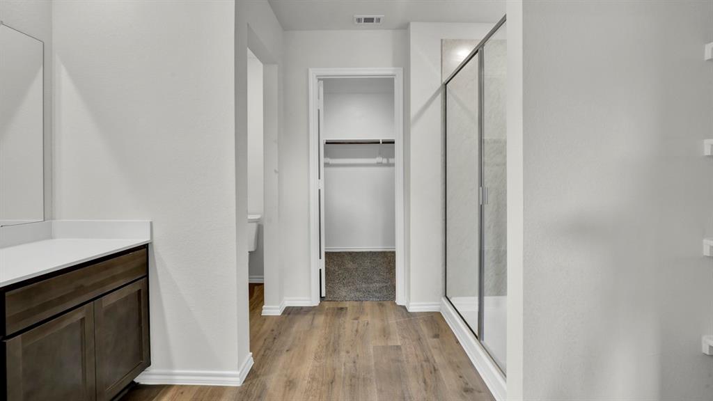 Bathroom with wood-finish flooring, a contemporary vanity with a white countertop, and a glass-enclosed shower