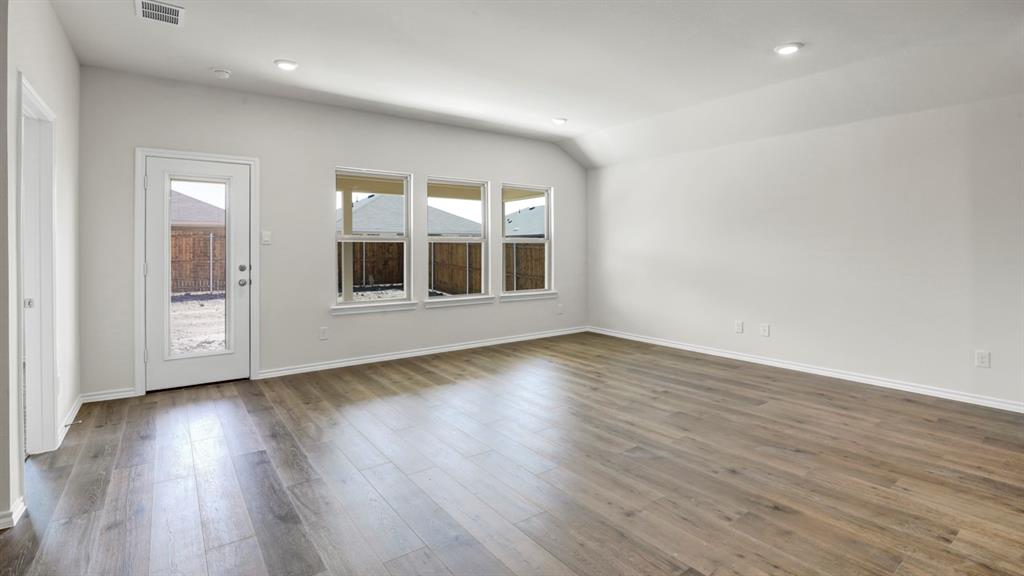 Spacious room featuring wood-finish flooring, vaulted ceilings, recessed lighting, and multiple windows