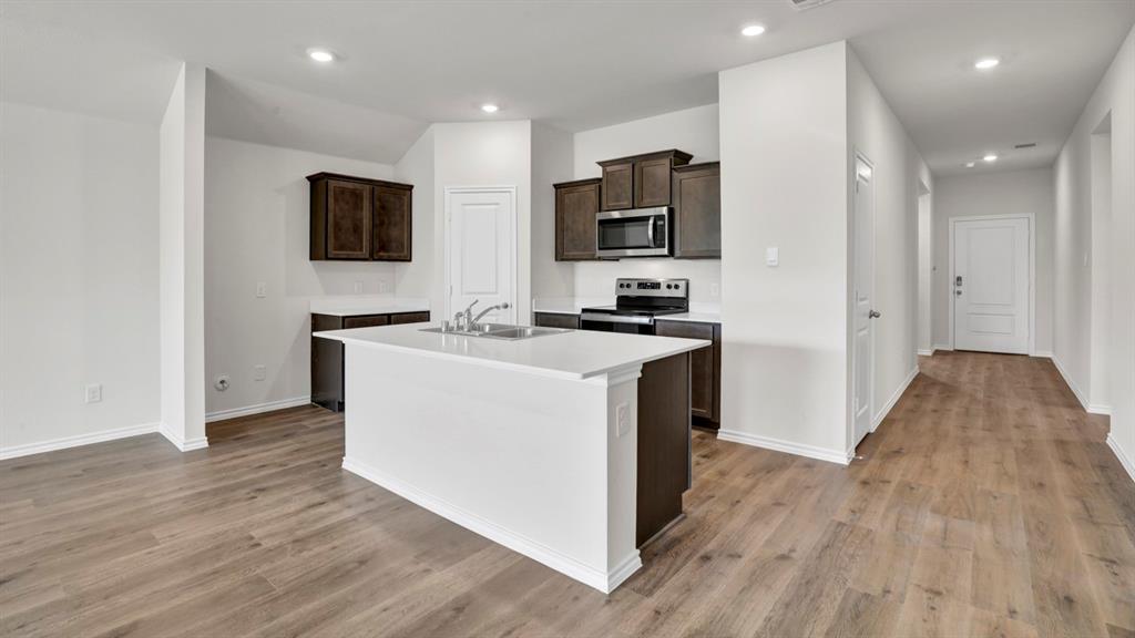 Contemporary kitchen featuring a central island with an undermount sink, dark wood cabinetry, stainless steel appliances, recessed lighting, and wood-finish flooring