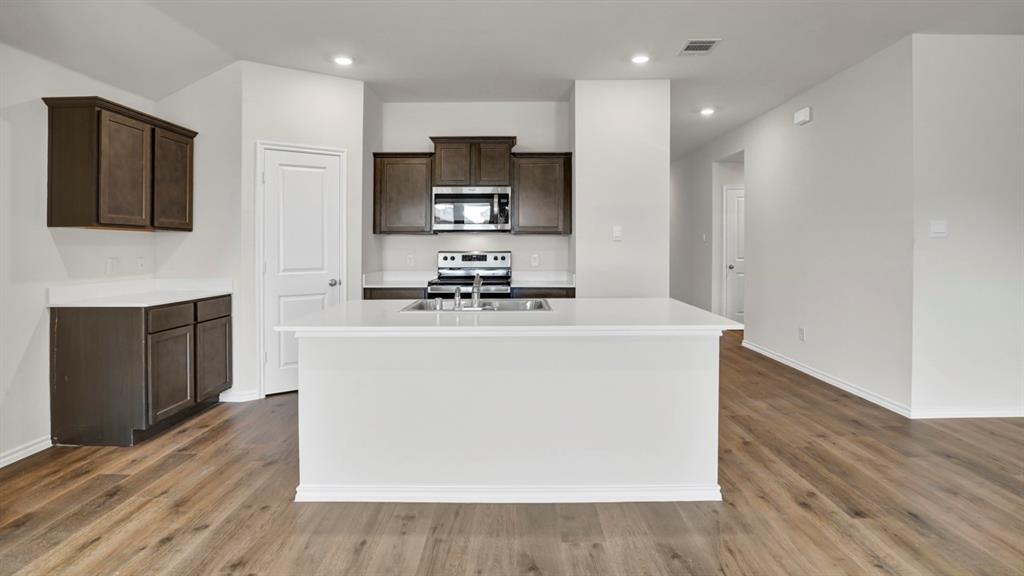 Open-concept kitchen featuring an expansive center island, dark wood-finish cabinetry, bright white countertops, stainless steel appliances, and wood-finish flooring