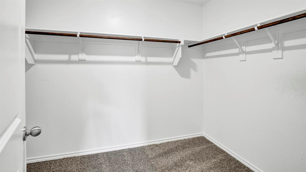Walk-in closet featuring white walls, gray carpet, and two levels of wood-finish hanging rods with shelving