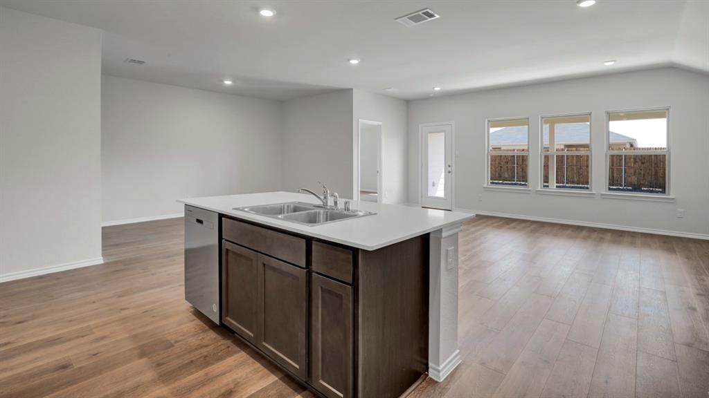 Kitchen island with dark wood cabinetry, a double basin sink, and a light-toned countertop