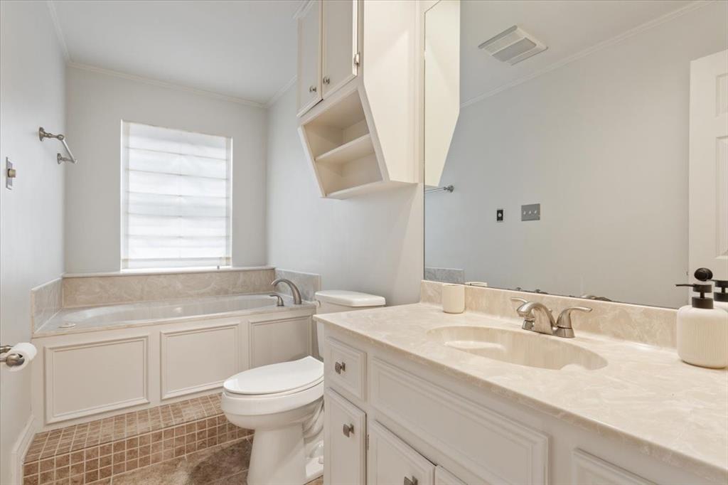 Bathroom featuring a built-in tub with a stone surround, a single vanity with stone countertop and integrated sink, a large wall-mounted mirror, and white cabinetry