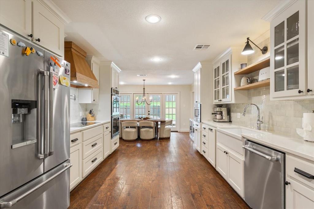 Kitchen featuring hardwood flooring, white cabinetry, stainless steel appliances, a farmhouse sink, and light-toned countertops