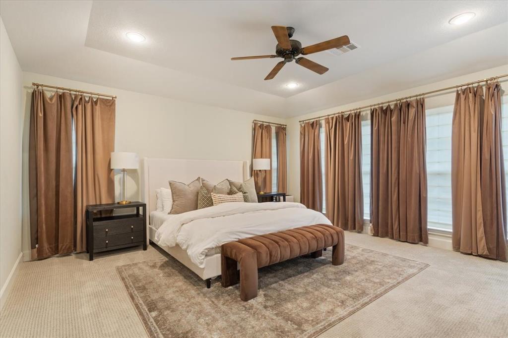 Spacious upstairs primary suite with tray ceiling, recessed lighting, and a five-blade ceiling fan