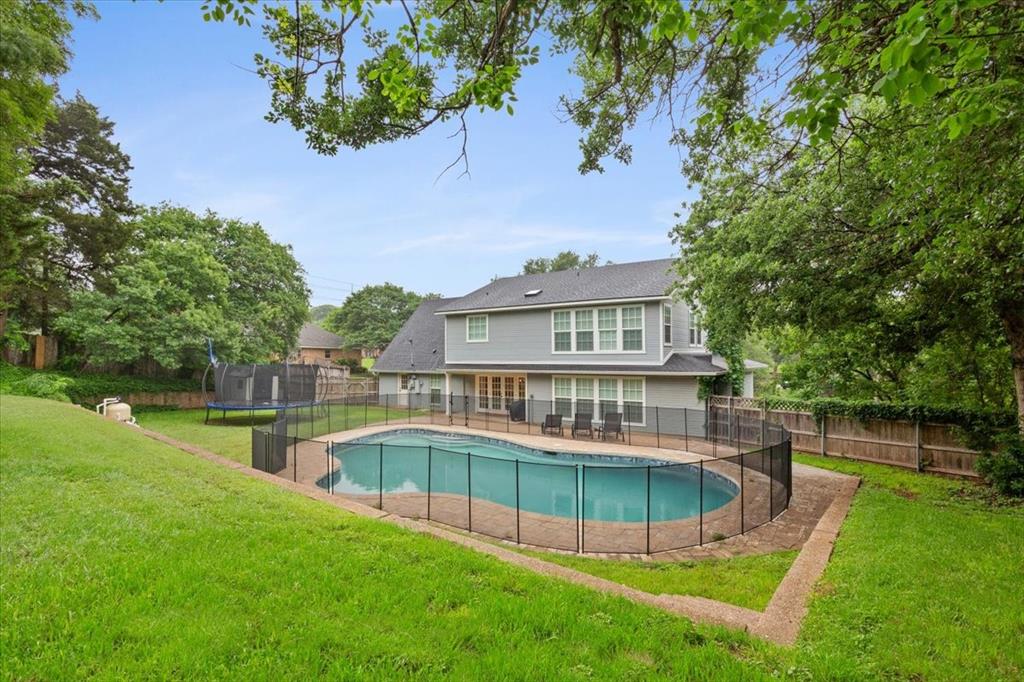 Spacious backyard featuring a fenced-in swimming pool with an integrated patio, extensive green lawn, and mature perimeter trees