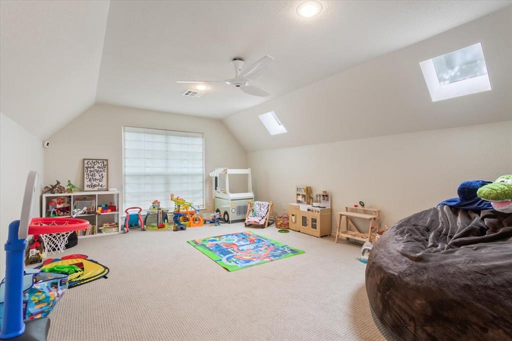 Upstairs carpeted room with a vaulted ceiling, multiple skylights, and a window with blinds