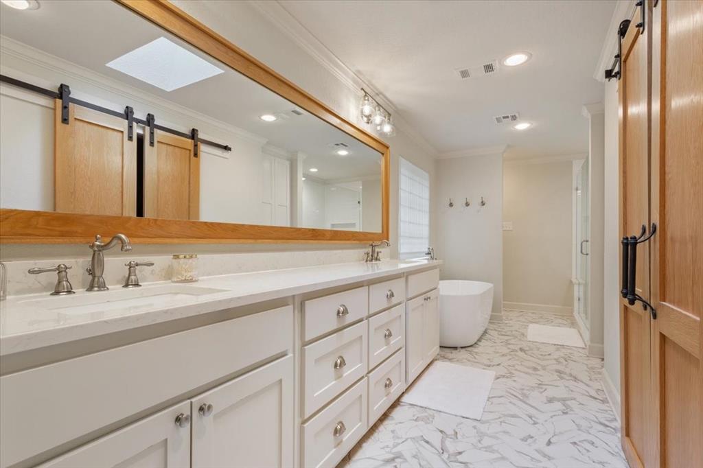 Upstairs bathroom featuring a dual vanity with white cabinetry and light-colored countertops, a freestanding soaking tub, and a glass-enclosed shower