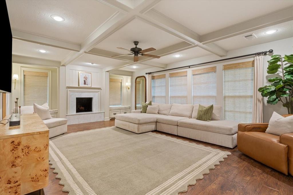 Spacious living area featuring a coffered ceiling, wood-finish flooring, and a fireplace with a stone surround Spacious living area featuring a coffered ceiling, wood-finish flooring, and a fireplace with a stone surround