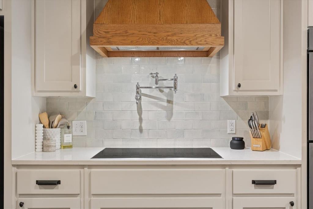 Induction cooktop with an integrated pot filler, surrounded by a light-colored subway tile backsplash and a custom wood range hood
