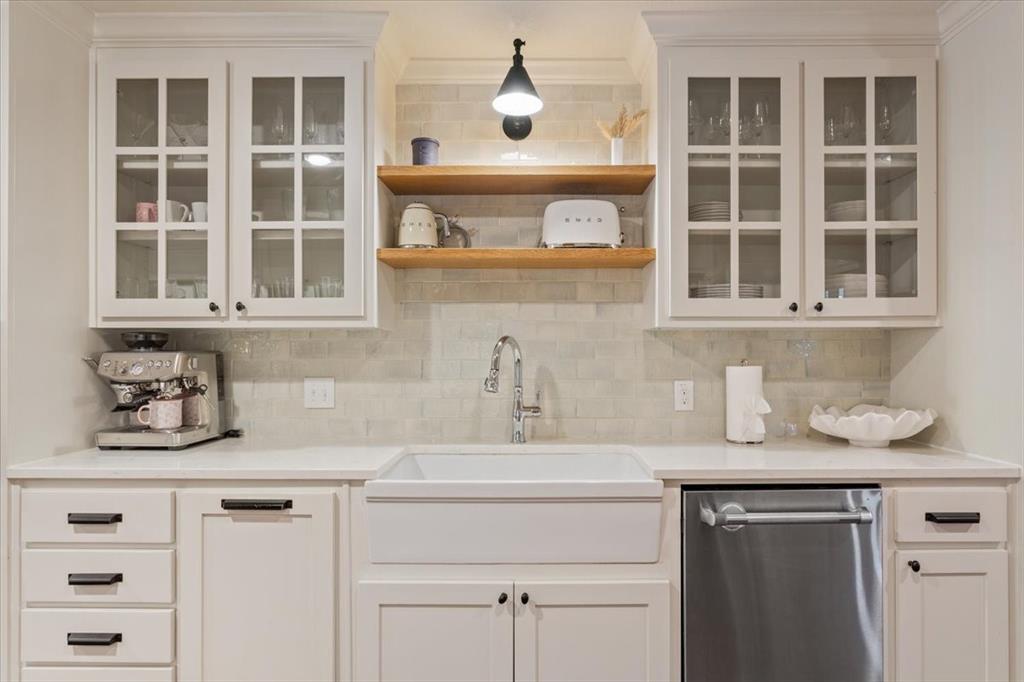 White shaker cabinetry with glass-front upper cabinets, a white farmhouse sink, and stainless steel dishwasher