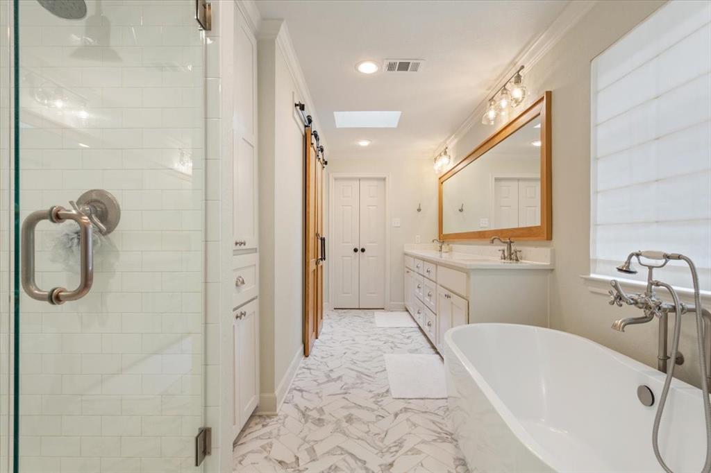 Upstairs freestanding soaking tub with floor-mounted fixture, dual vanity with undermount sinks, and a large framed mirror with overhead lighting