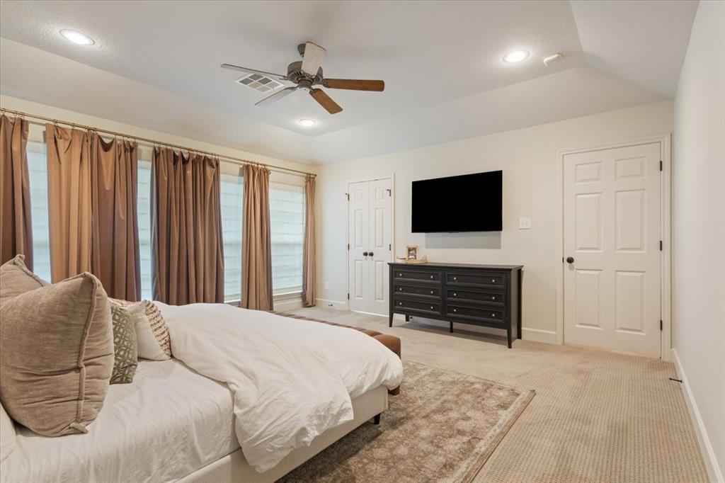 Upstairs carpeted primary suite featuring a tray ceiling with recessed lighting and a ceiling fan