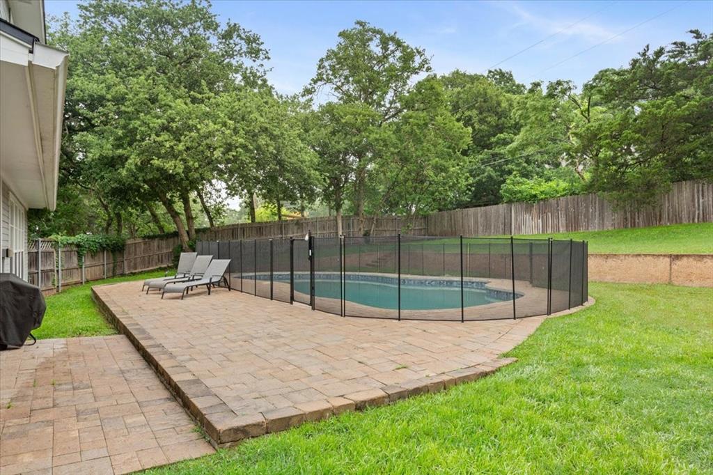 Backyard featuring a paver patio with a fenced-in swimming pool, surrounded by a grassy lawn and mature trees
