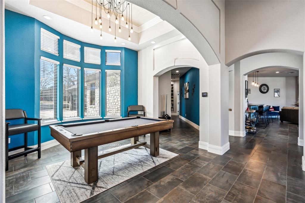 Spacious entertainment area featuring a curved bay window, modern chandelier, dark tile flooring, and arched doorways