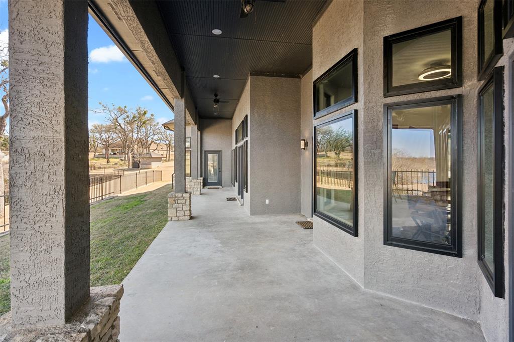 Expansive covered patio featuring a concrete surface, stucco columns with stone bases, black-framed windows, and recessed lighting