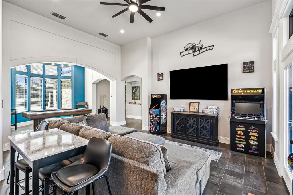 Spacious entertainment room featuring dark tile flooring, a built-in media console, ceiling fan, recessed lighting, and a large arched entryway leading to an additional space with expansive windows