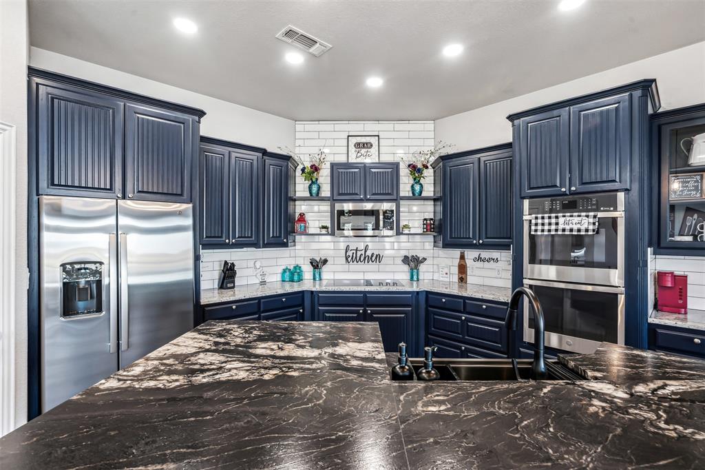 Kitchen featuring dark cabinetry, stainless steel appliances, a subway tile backsplash, recessed lighting, and a kitchen island with a dark sink and faucet
