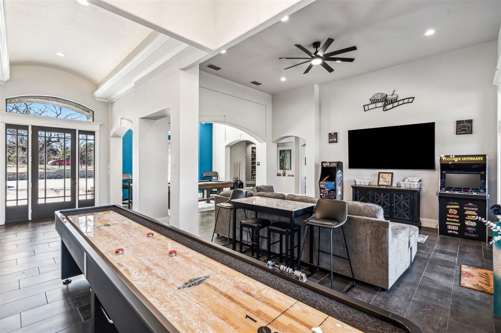 Spacious entertainment room featuring dark wood-finish flooring, high ceilings with recessed lighting, and a modern ceiling fan