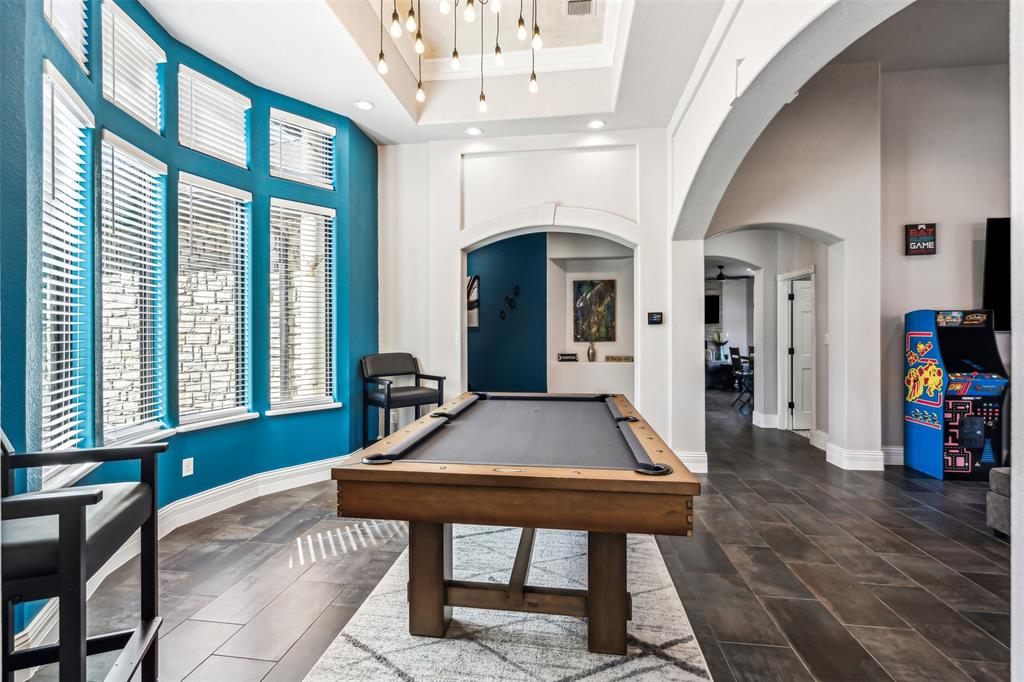 Game room featuring a billiard table, a curved wall of multiple windows with blinds, wood-finish flooring, a tray ceiling with pendant lighting, and multiple arched doorways