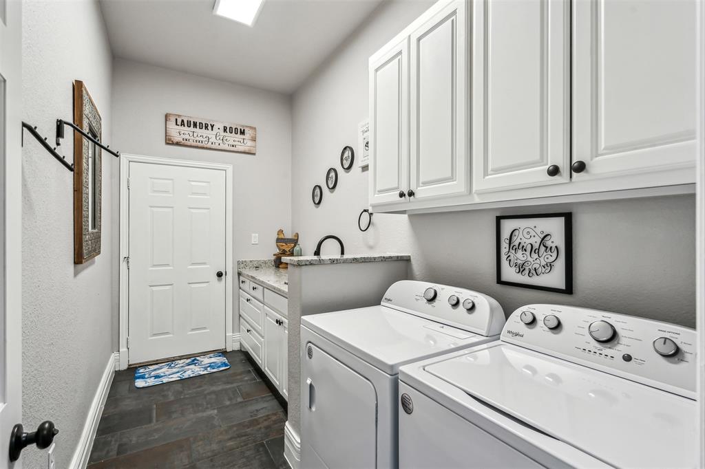 Dedicated laundry room featuring dark tile flooring, white shaker cabinetry, a granite-finish countertop with a built-in sink, and overhead recessed lighting