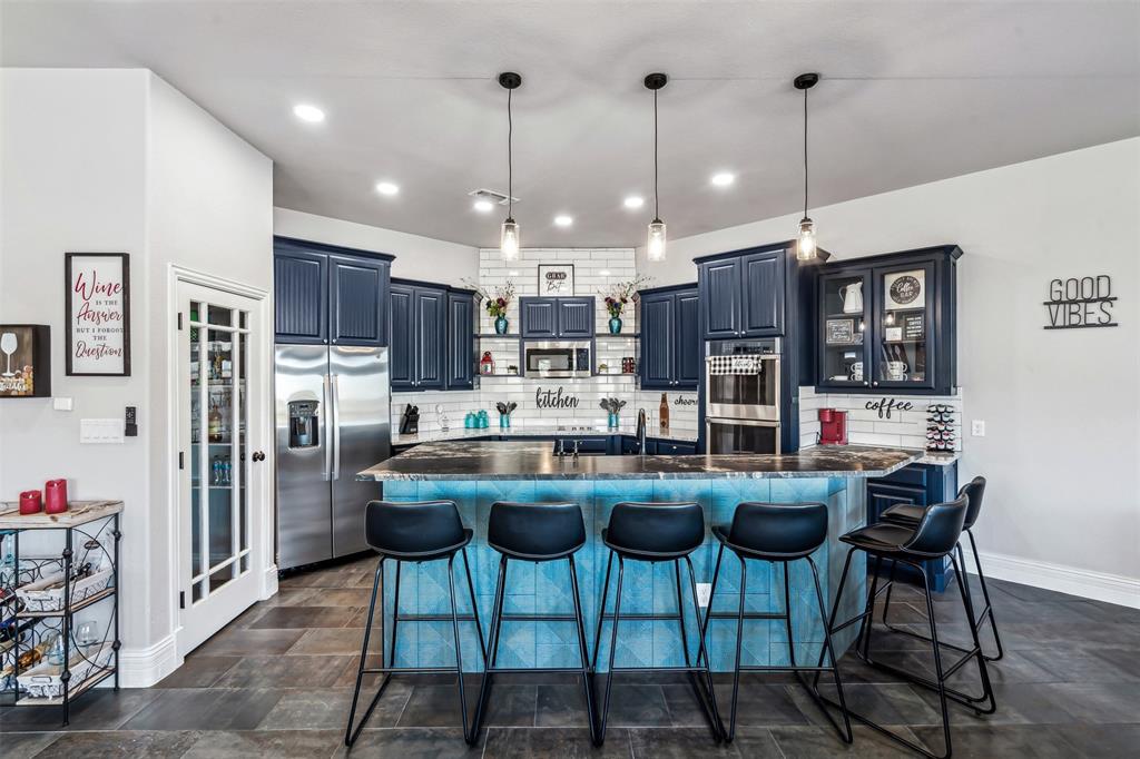 Modern kitchen featuring dark blue cabinetry, subway tile backsplash, stainless steel appliances, a multi-level island with seating, and pendant lighting