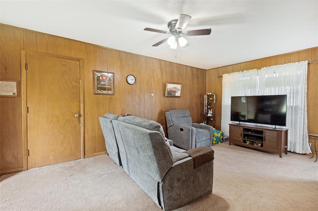 Living space featuring wood paneling, light-colored carpeting, a white ceiling, and a ceiling fan with integrated lighting