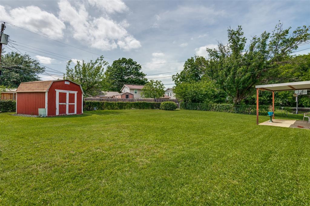 Expansive backyard featuring a manicured lawn, established shrubbery, a red storage shed, and a covered patio area