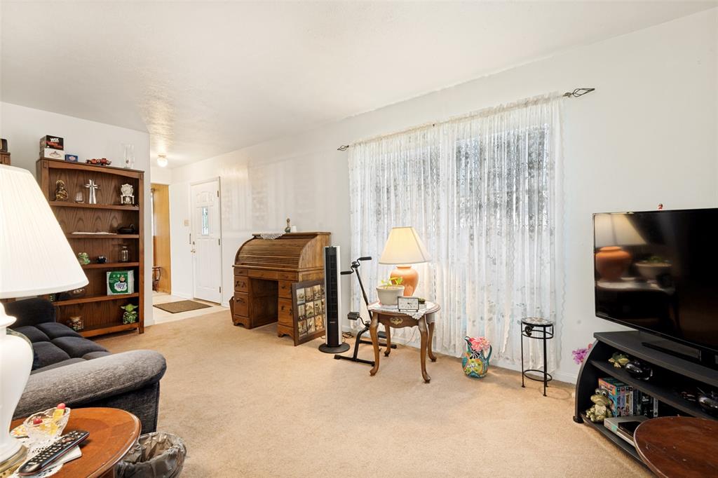 Carpeted living area featuring a large window with sheer curtains, a built-in bookcase, and a white entry door