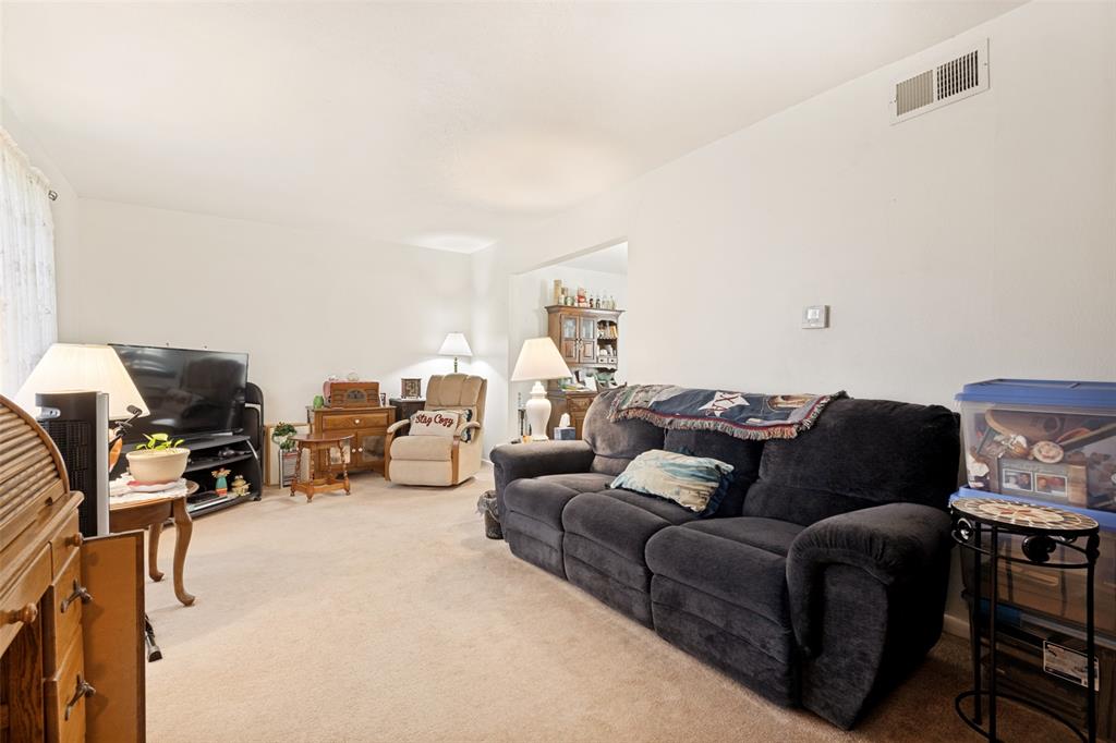 Carpeted living area featuring light-toned walls and an overhead air vent