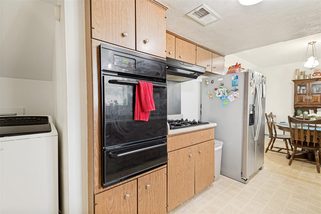Kitchen featuring wood-finish cabinetry, a built-in double oven, a gas cooktop with an overhead range hood, a stainless steel refrigerator, and tiled flooring