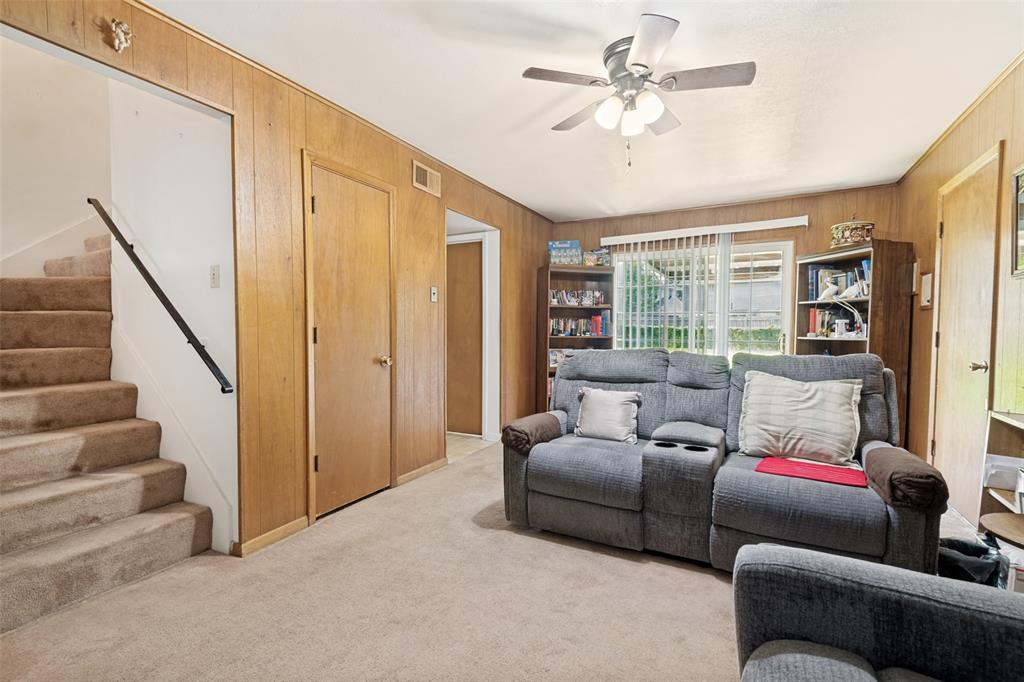 Living area featuring wood-finish wall paneling, carpeted flooring, and a ceiling fan