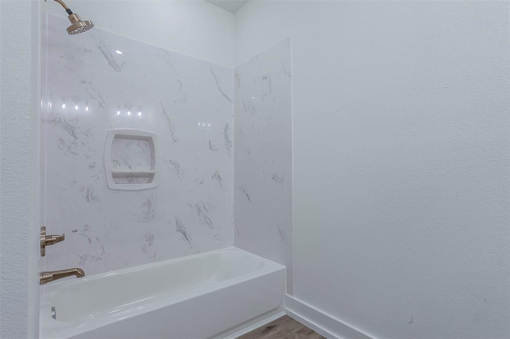 Bathroom featuring a white tub, white faux-marble shower surround, integrated shower niche, and brushed brass fixtures