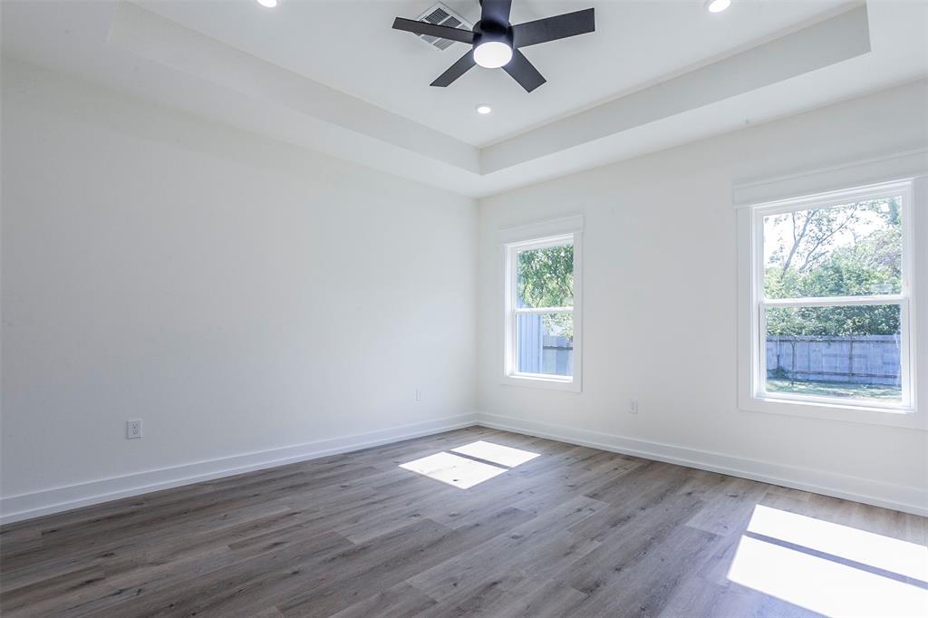 Bright room featuring wood-finish flooring, two large windows, a tray ceiling, recessed lighting, and a ceiling fan