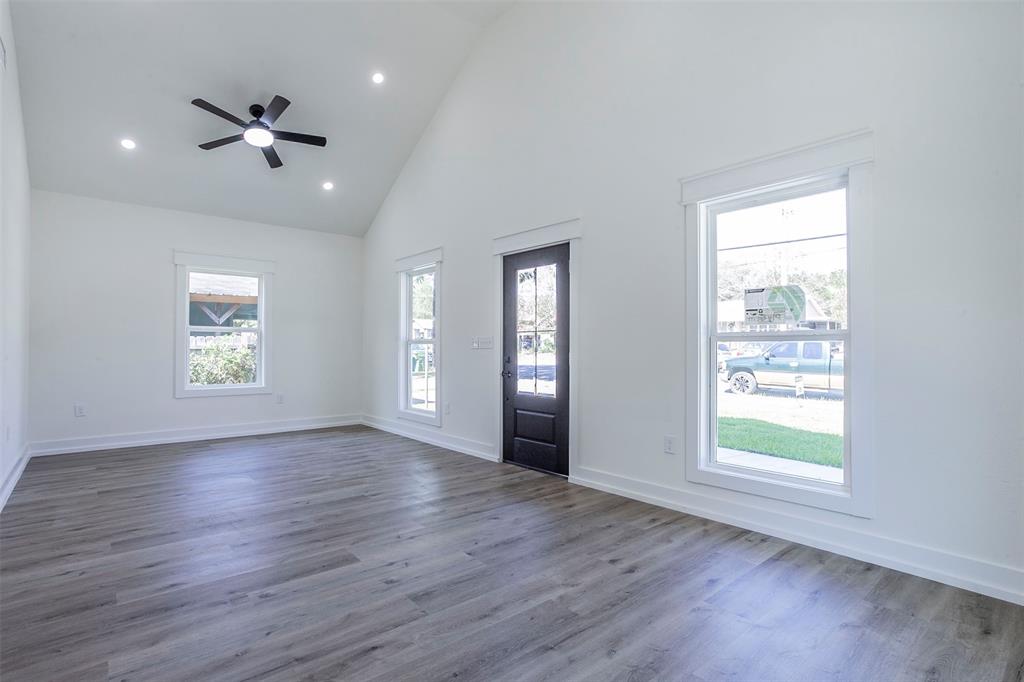 Spacious interior featuring a vaulted ceiling with a ceiling fan, recessed lighting, wood-finish flooring, white baseboards, and white window trim