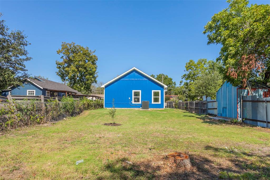 Spacious backyard featuring a vibrant blue exterior, white trim windows, and mature trees