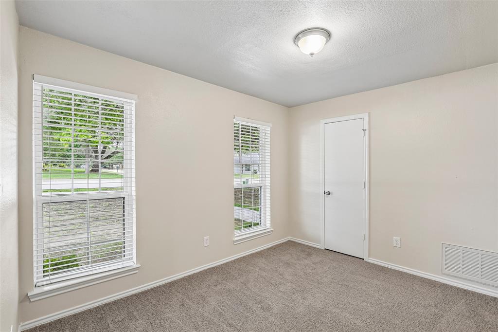 Neutral-toned interior room featuring two windows with white blinds, carpet flooring, a white door with a silver knob, and a ceiling-mounted light fixture