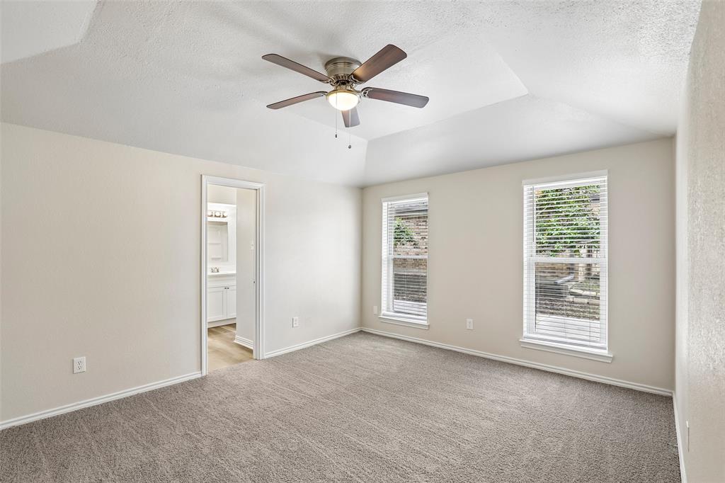 Spacious room featuring a tray ceiling, ceiling fan with integrated lighting, and two windows with blinds