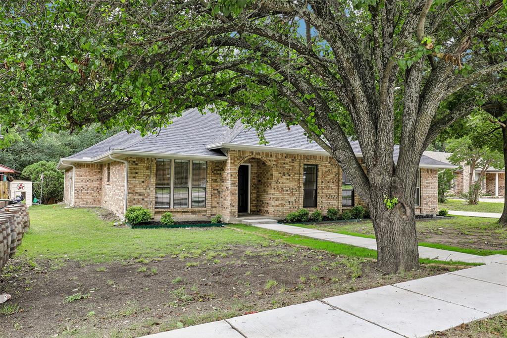 Brick exterior with a dark shingle roof, featuring mature trees providing ample shade