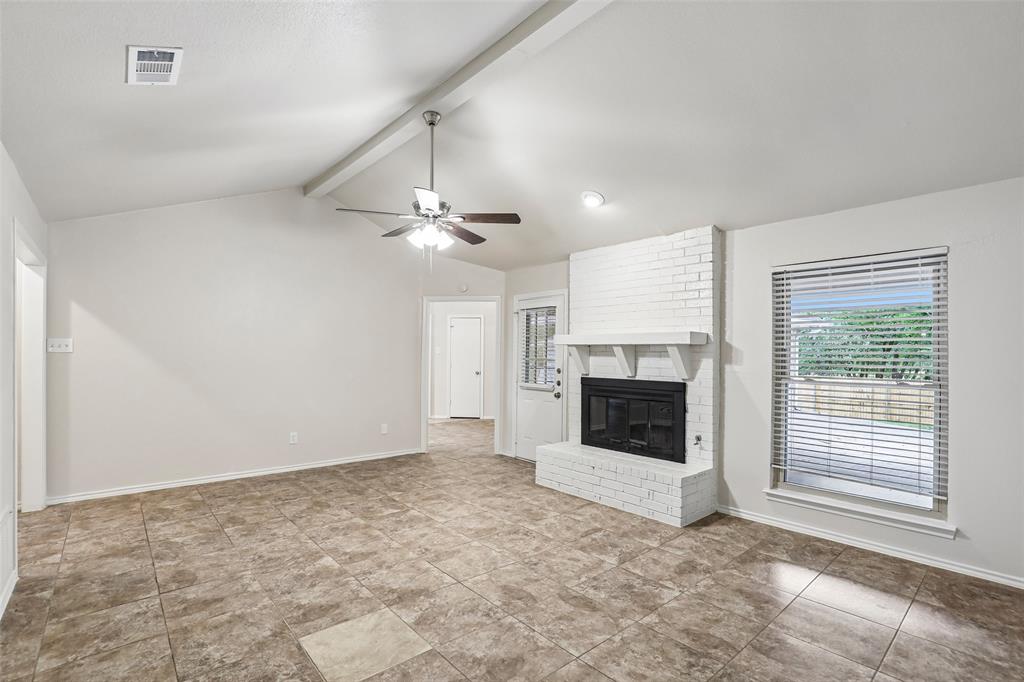 Spacious living area featuring vaulted ceilings, a white brick fireplace, and durable tile flooring