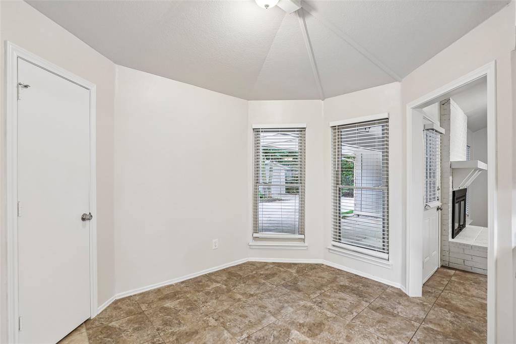 Bay window area featuring two windows with blinds, a vaulted ceiling, and neutral-toned tile flooring