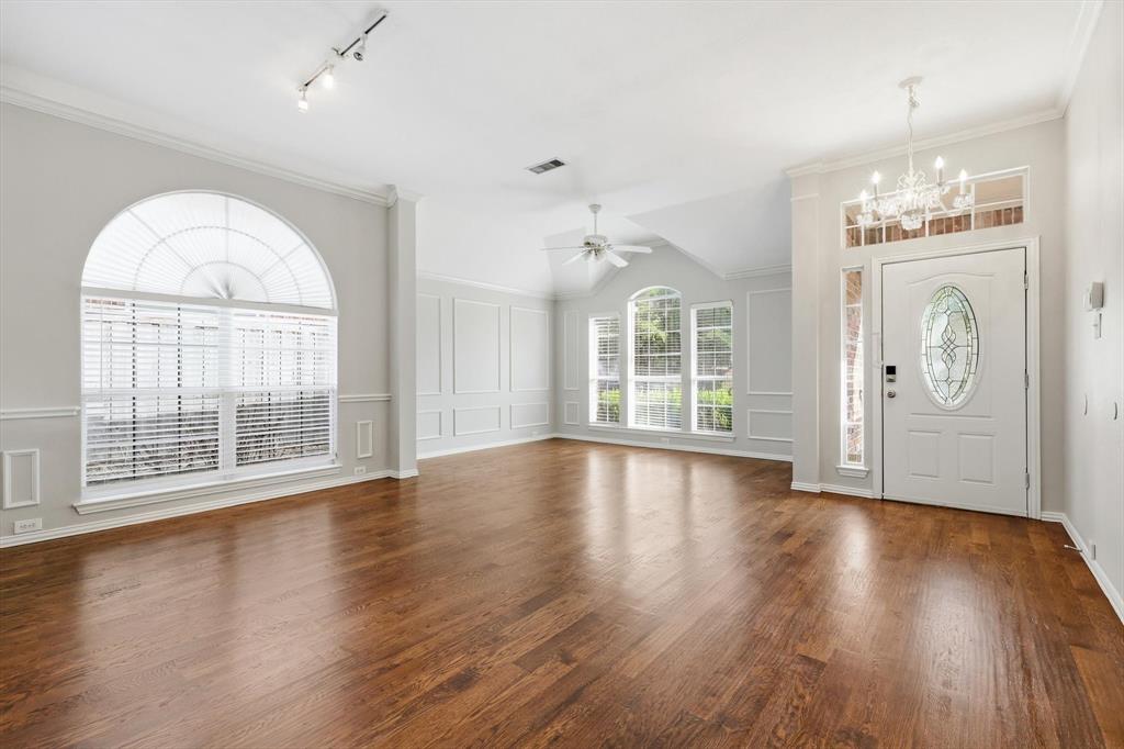 Entryway and living area featuring wood-finish flooring, an arched window with blinds, decorative wall paneling, a vaulted ceiling, and a white front door with an oval leaded glass insert