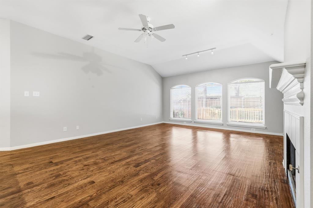 Spacious room featuring vaulted ceilings, wood-finish flooring, and a fireplace with a decorative mantel