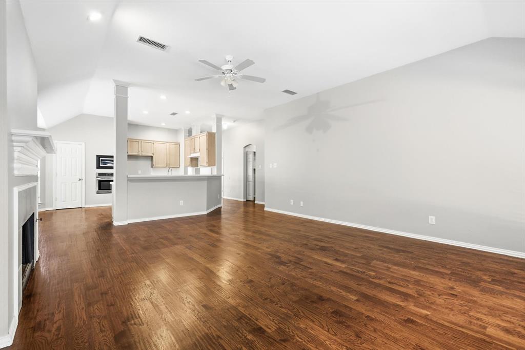 Spacious living area featuring wood-finish flooring, a white mantelpiece, vaulted ceilings, and a ceiling fan