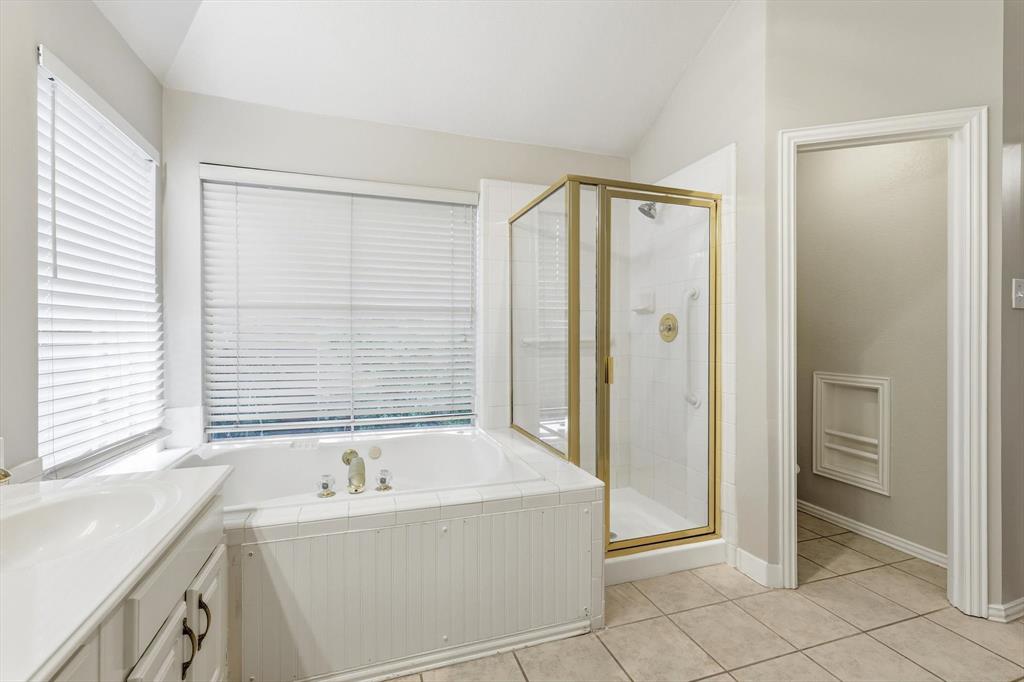 Neutral-toned bathroom featuring a built-in tub with tile surround, a separate shower with a gold-framed glass enclosure, and a vanity with a white countertop