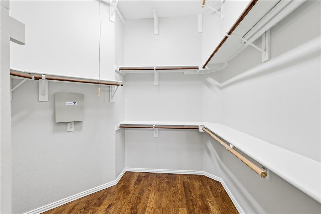 Walk-in closet featuring wood-finish flooring, white walls, white shelving, and hanging rods