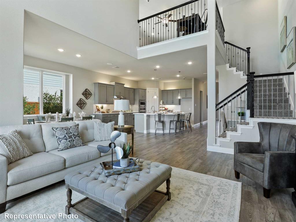 Open-concept living area featuring high ceilings, wood-finish flooring, a two-story staircase with wrought iron balusters, a kitchen with grey cabinetry and an island, and a dining area with ample natural light