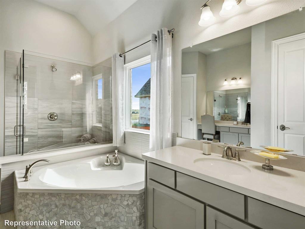 Bathroom featuring a corner soaking tub with pebble-tile surround, a glass-enclosed shower with tile walls, a vanity with a drop-in sink and ample counter space, and a separate vanity area