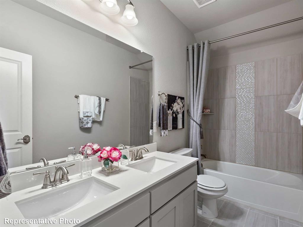 Bathroom featuring a dual vanity with undermount sinks and brushed nickel fixtures, a tub/shower combination with subway tile surround, a decorative mosaic tile accent, and light gray tile flooring