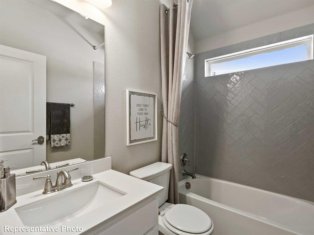 Bathroom featuring a vanity with an integrated sink, a large mirror, and a bathtub with a tiled surround